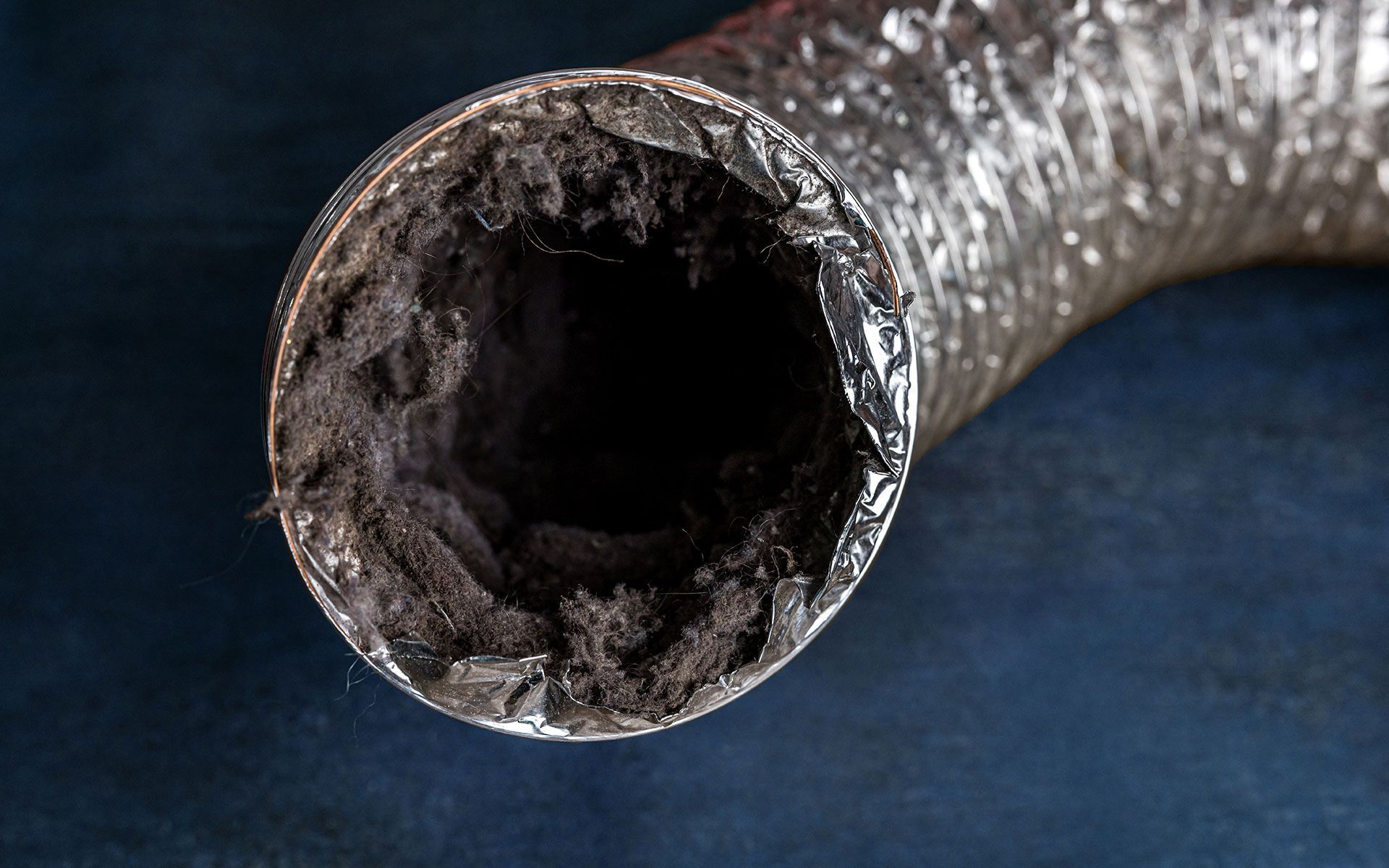 Clogged, flexible ductwork interior, dark with debris buildup, shiny silver exterior.