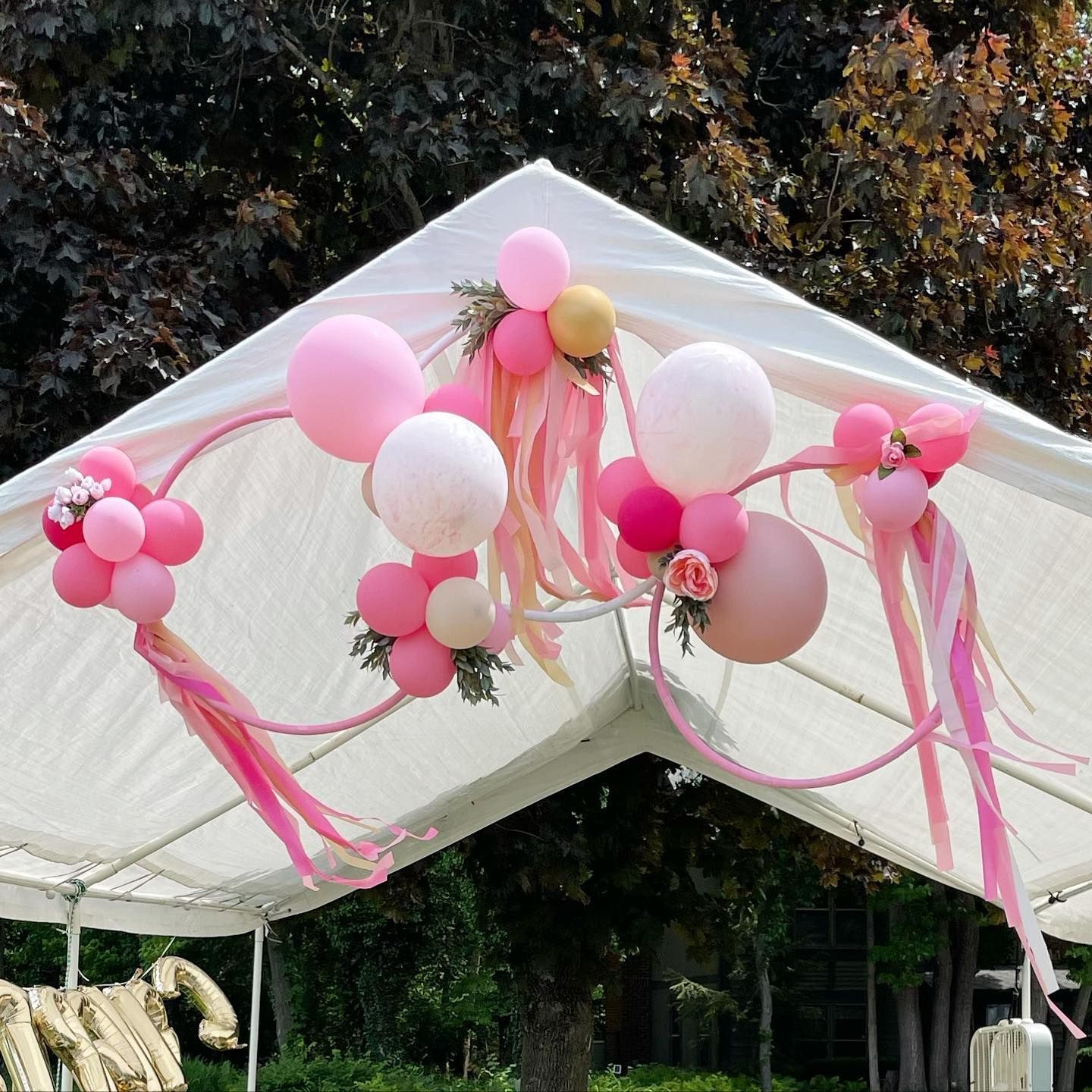A white tent is decorated with pink balloons and ribbons.