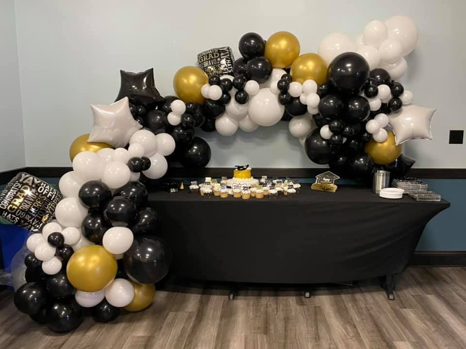 A table decorated with black, white, and gold balloons and a cake.