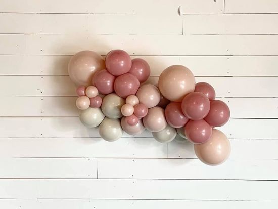 A bunch of pink and white balloons are hanging on a white wooden wall.