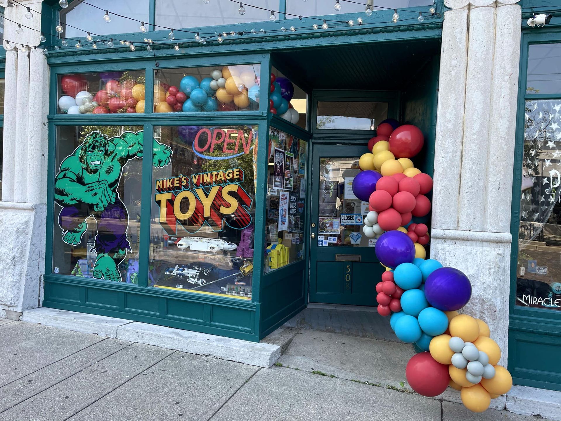 A store front with balloons and a sign that says open.