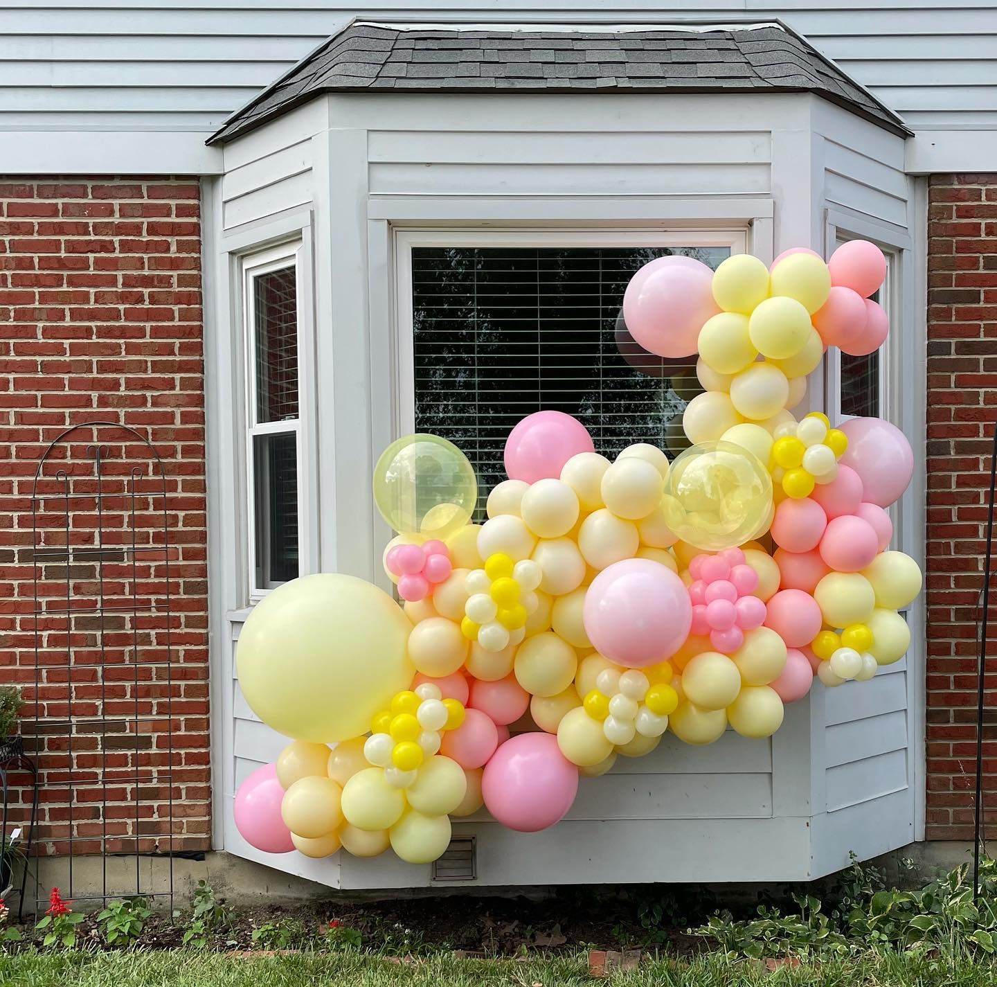 A bunch of pink and yellow balloons in front of a window.