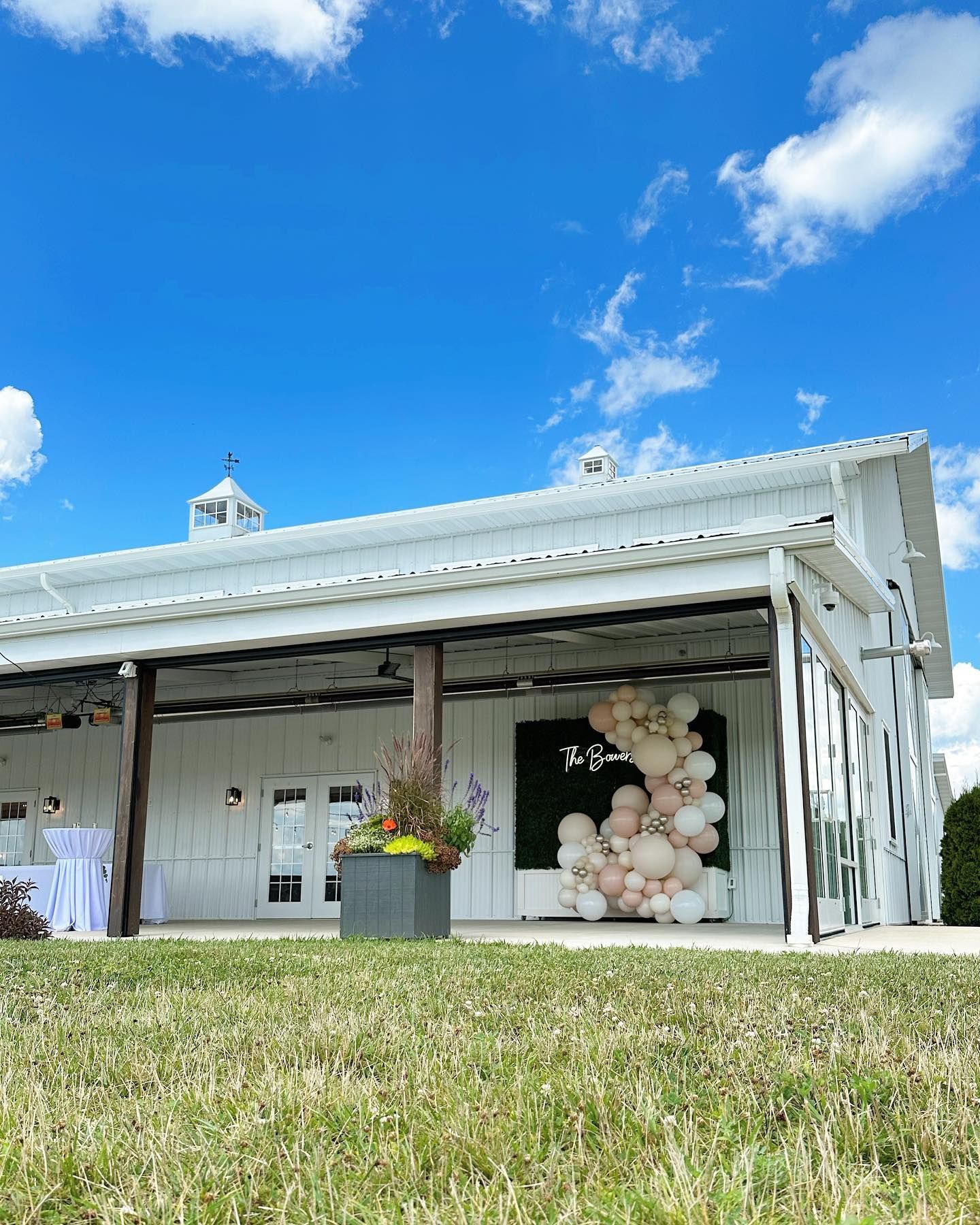 A white barn with balloons on the porch is sitting on top of a lush green field.