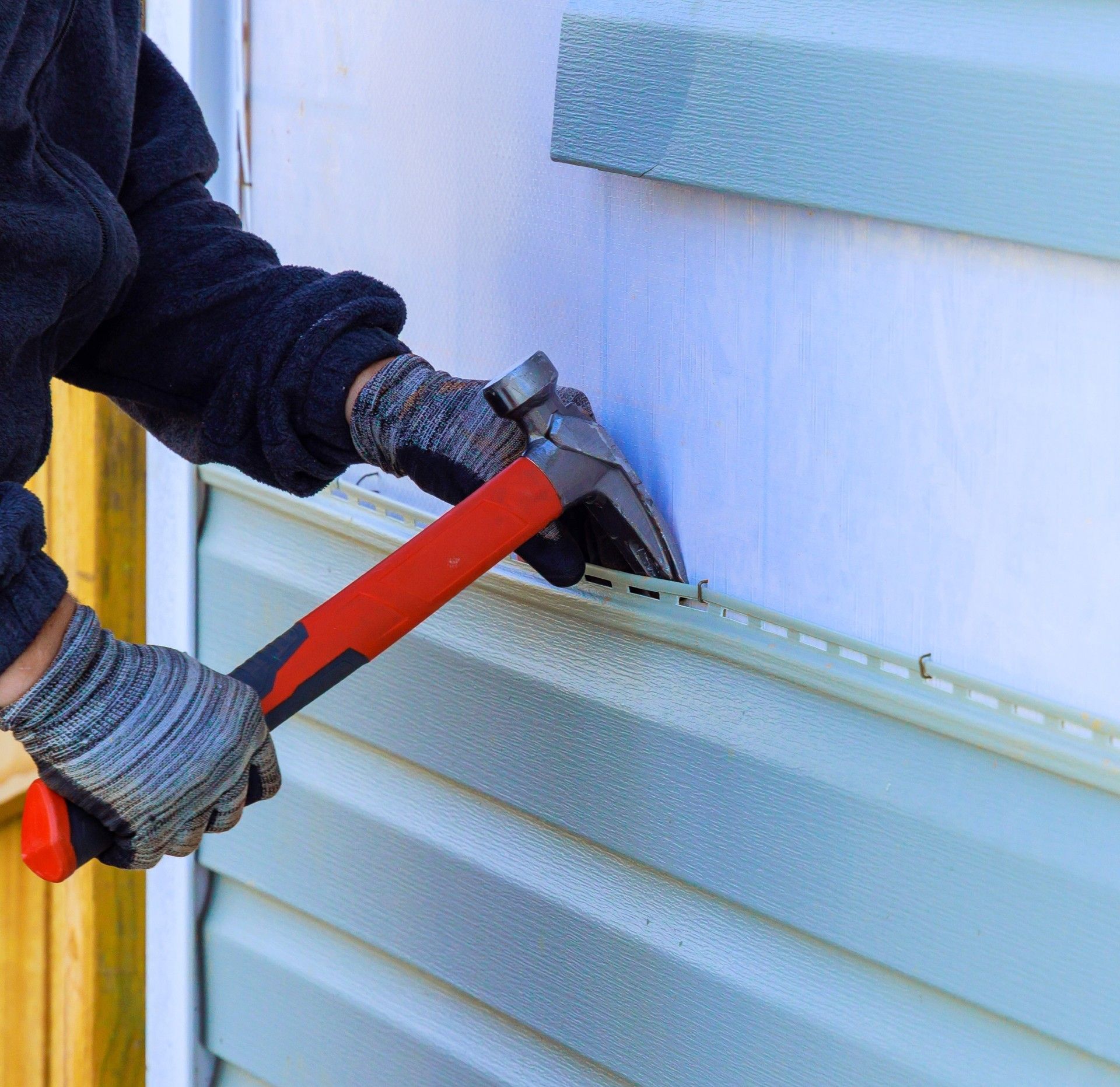 A person is installing siding on a house with a hammer.