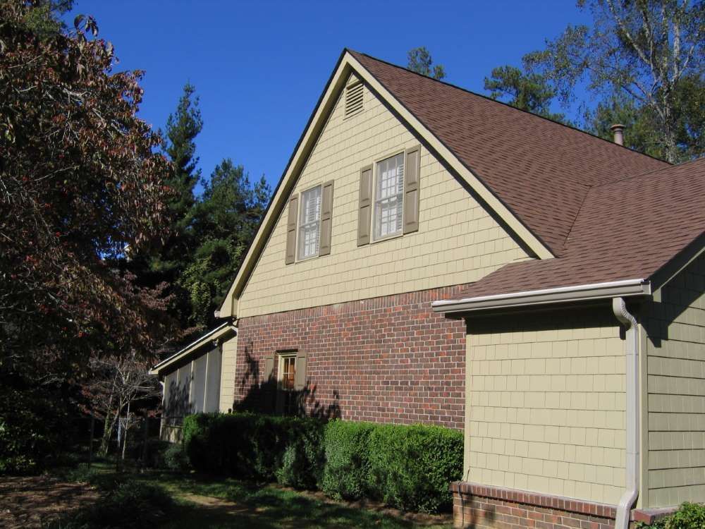 A brick house with a tan siding and a brown roof