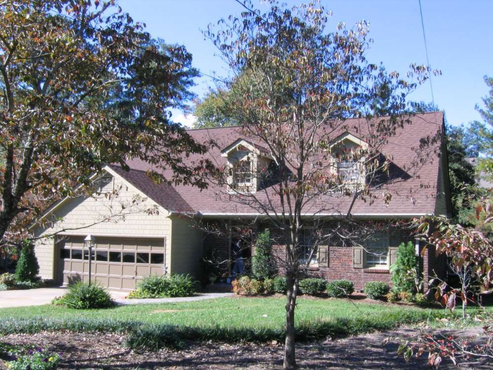 A house with a brown garage door is surrounded by trees