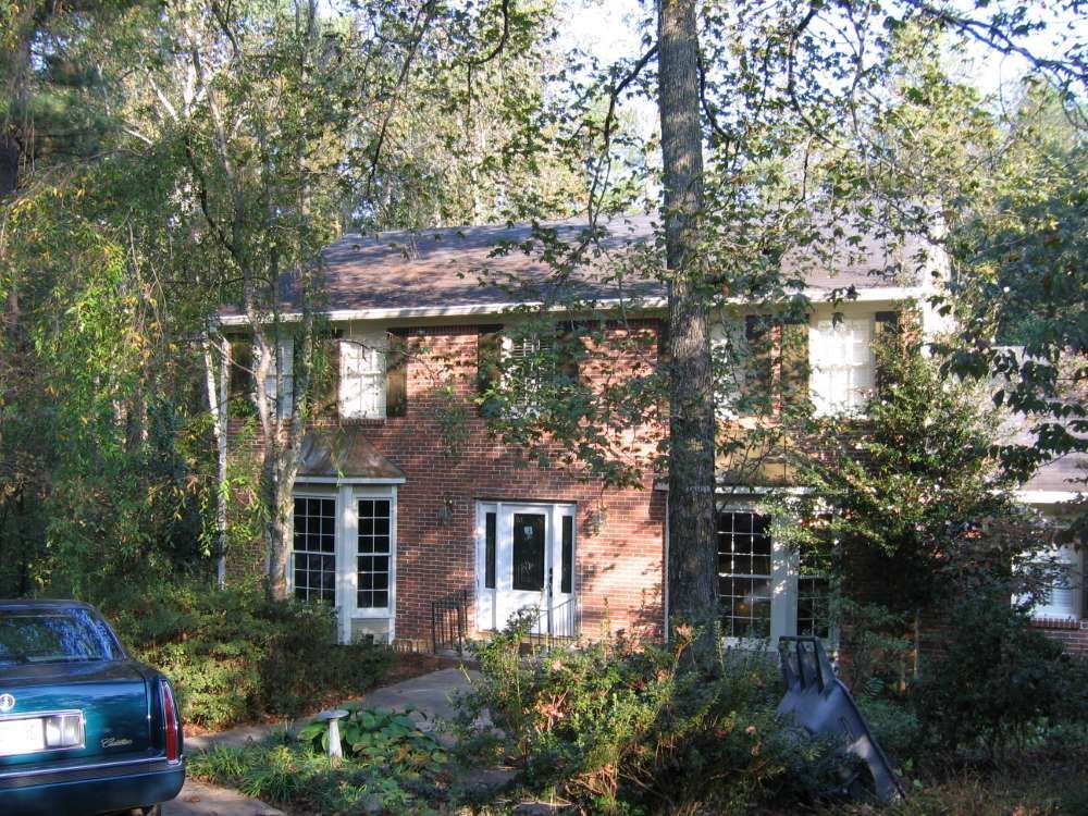 A blue car is parked in front of a brick house