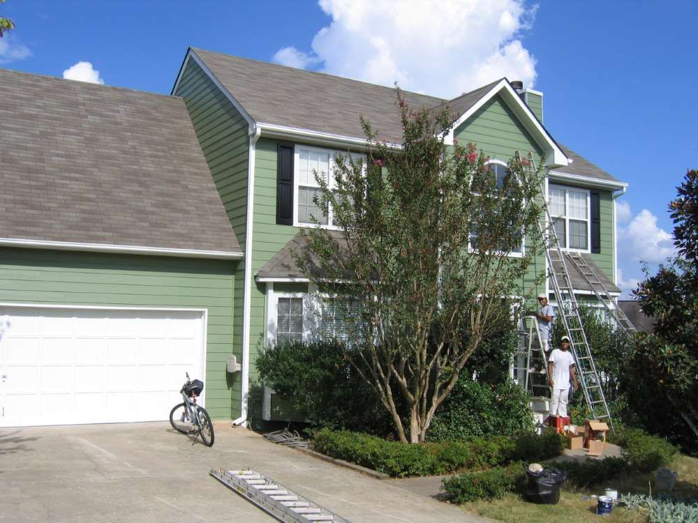 A green house is being painted by a man on a ladder