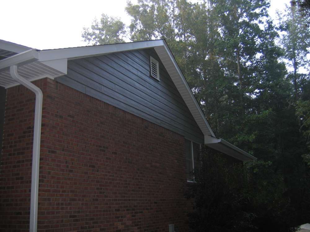 A brick house with a gray siding and a white gutter