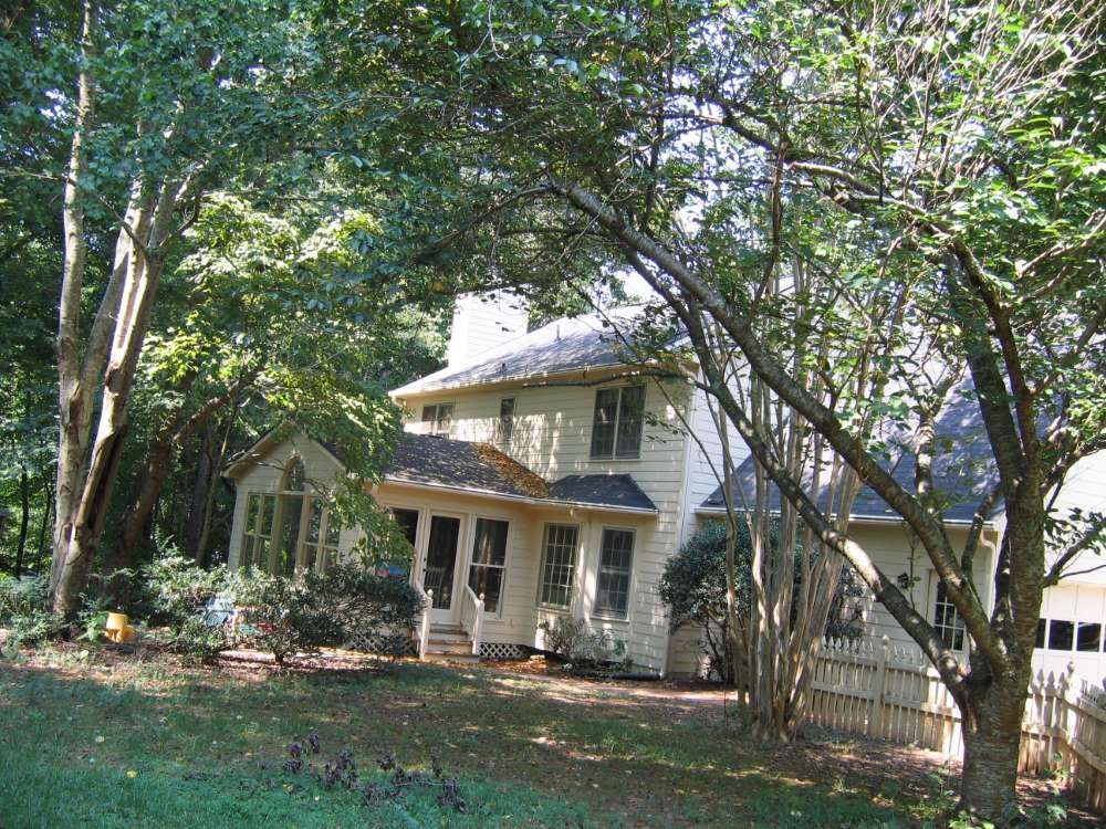 A white house with a black roof is surrounded by trees