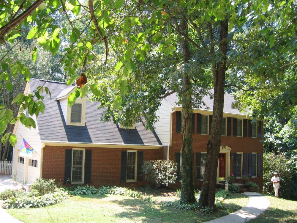A brick house with black shutters is surrounded by trees