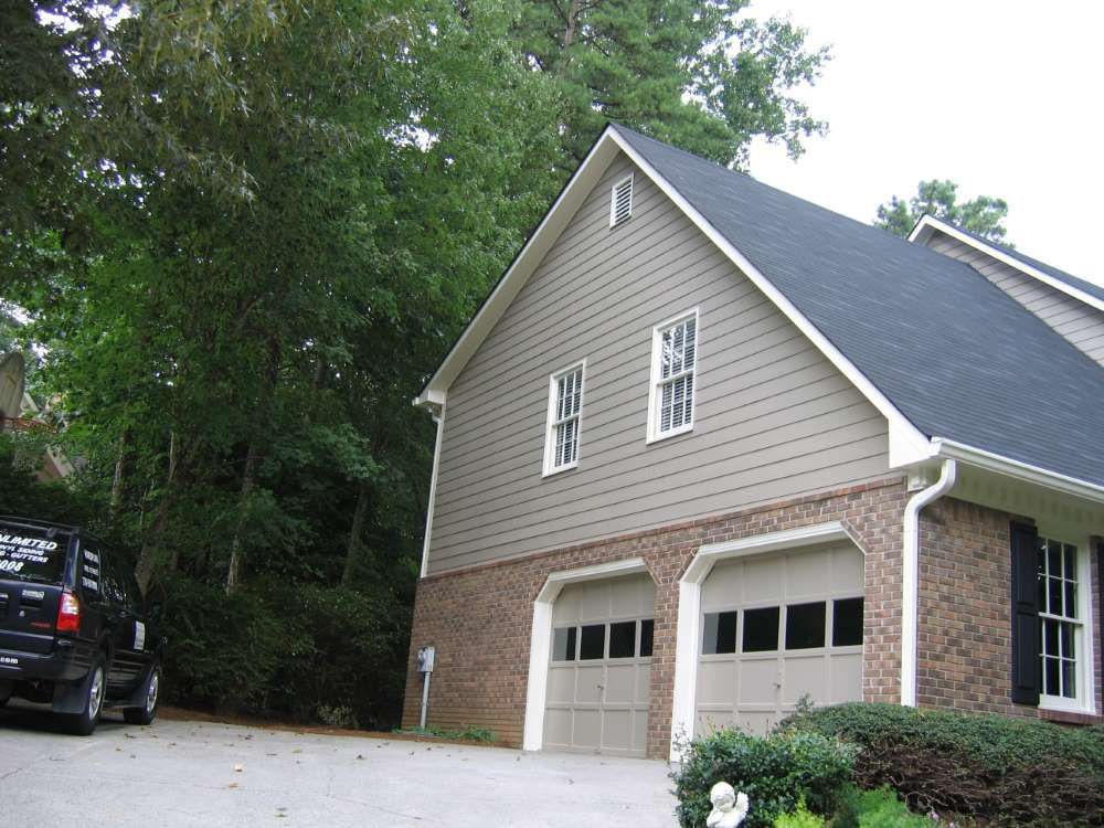 A car is parked in front of a house with two garage doors