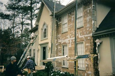 A man is standing on a ladder in front of a house that is being painted