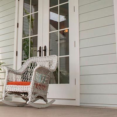 A white wicker rocking chair is sitting on a porch in front of a white door.