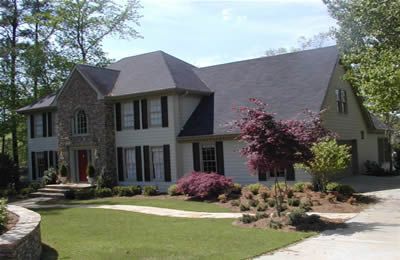 A large white house with black shutters is surrounded by trees and grass.