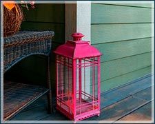 A pink lantern is sitting on a porch next to a wicker table.
