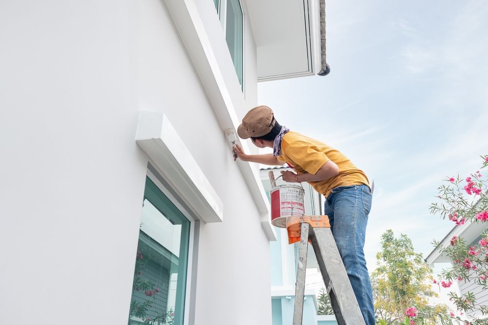 A man is standing on a ladder working on the side of a house.