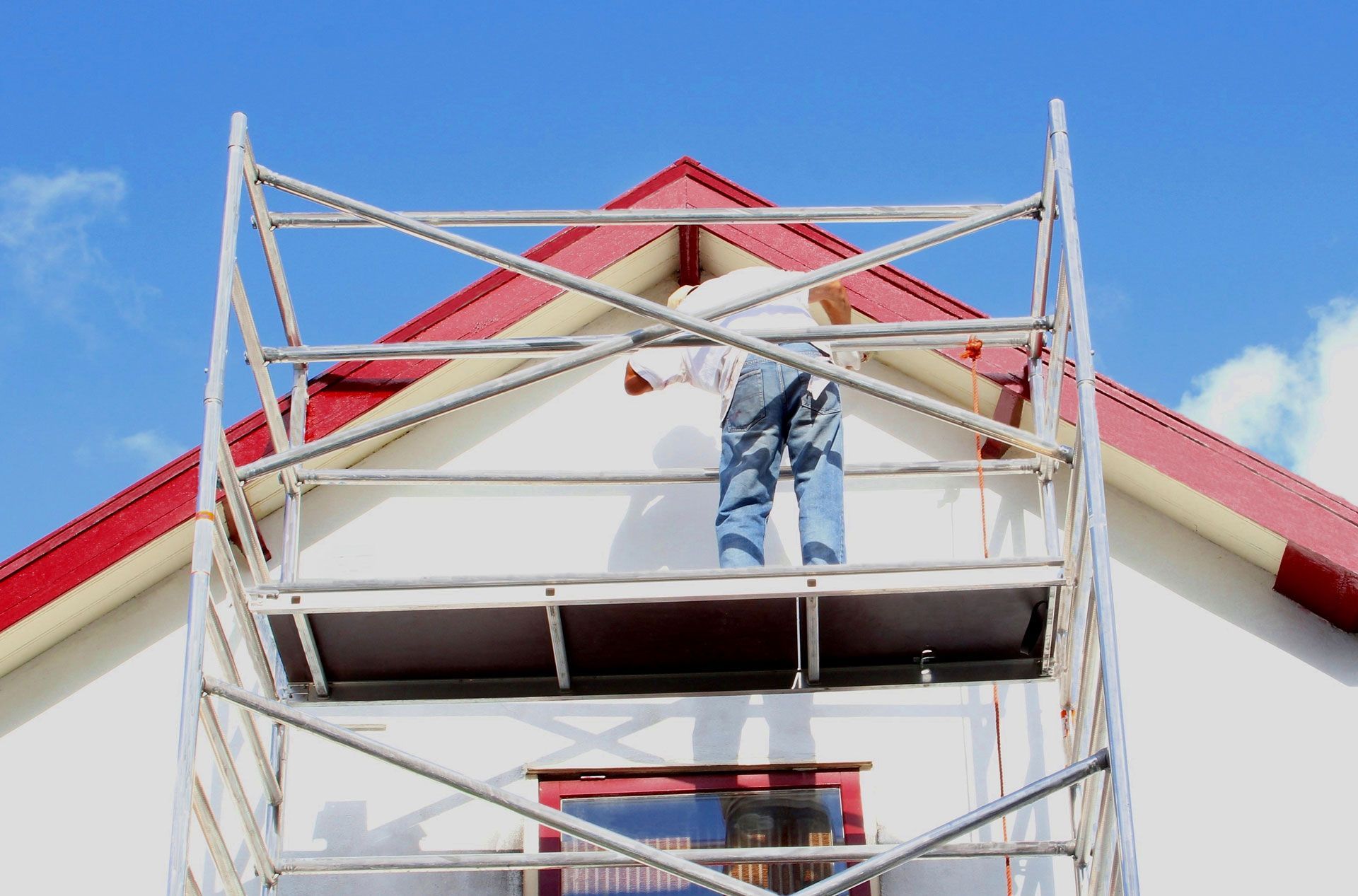 A man is painting the side of a house on a scaffolding.