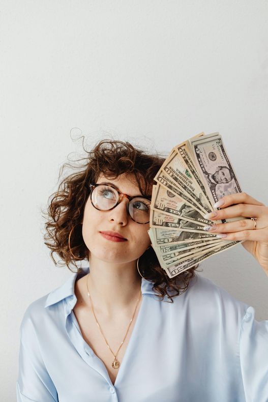 A woman is holding a fan of money in front of her face.