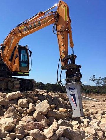 A yellow excavator breaking rocks