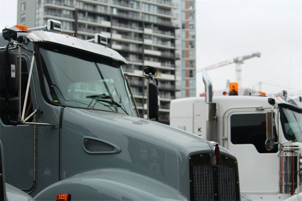 A row of semi trucks are parked in front of a tall building