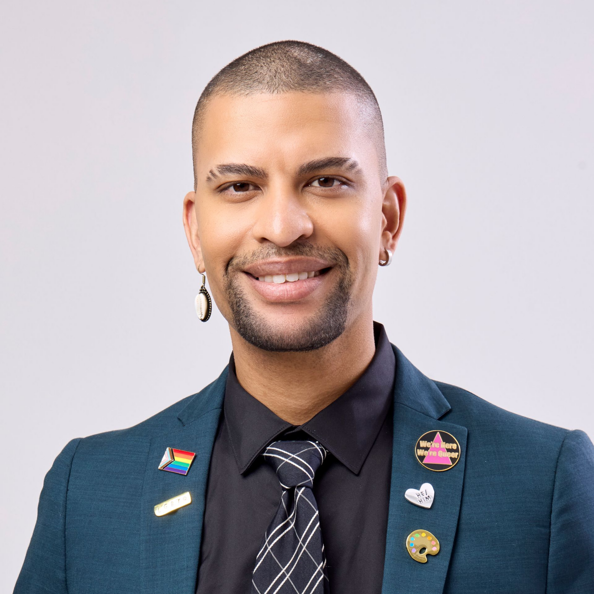 Man in teal blazer and black tie smiling, wearing pins.