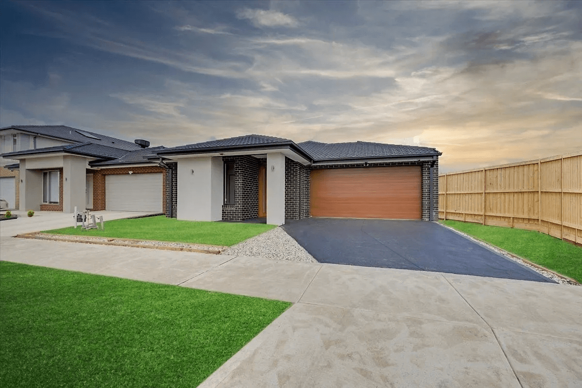 A modern brick house with large windows and a covered patio sits in a fenced backyard with bright green grass on Denmead Drive, Donnybrook, VIC 3064, under a partly cloudy sky.