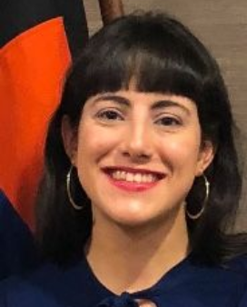 Woman with dark hair and bangs smiles, wearing hoop earrings and a navy top.