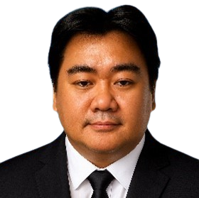 Man in a black suit and tie, smiling slightly, against a white background.