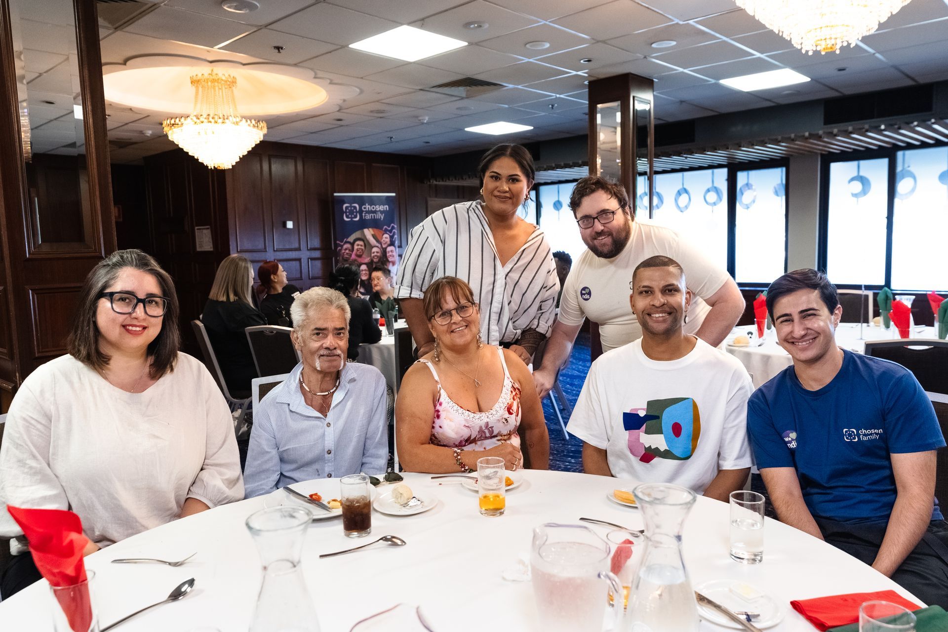 Group of people seated at a round table in a dining room, smiling at the camera.
