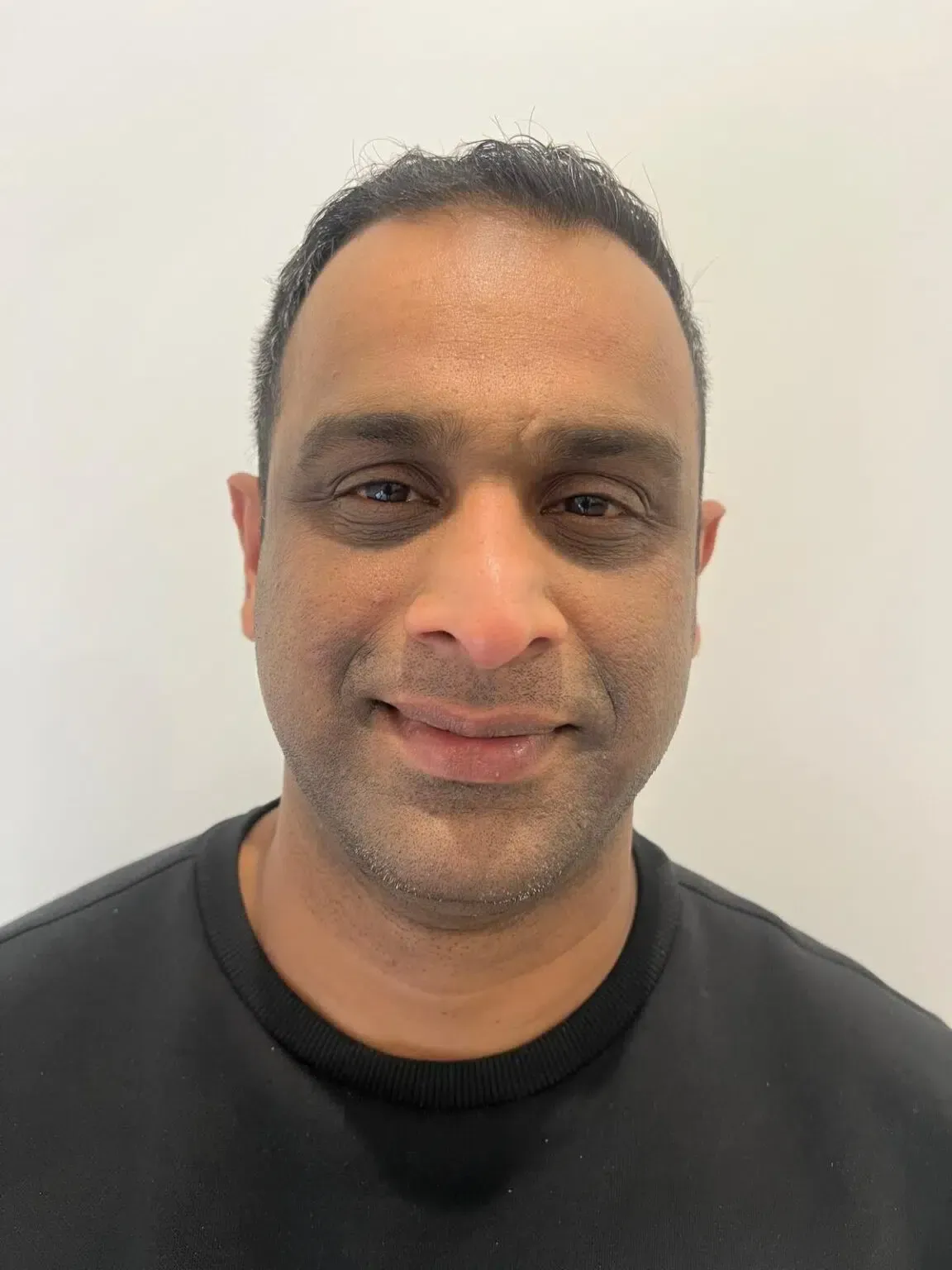 Man wearing a black shirt, smiling at the camera against a white background.