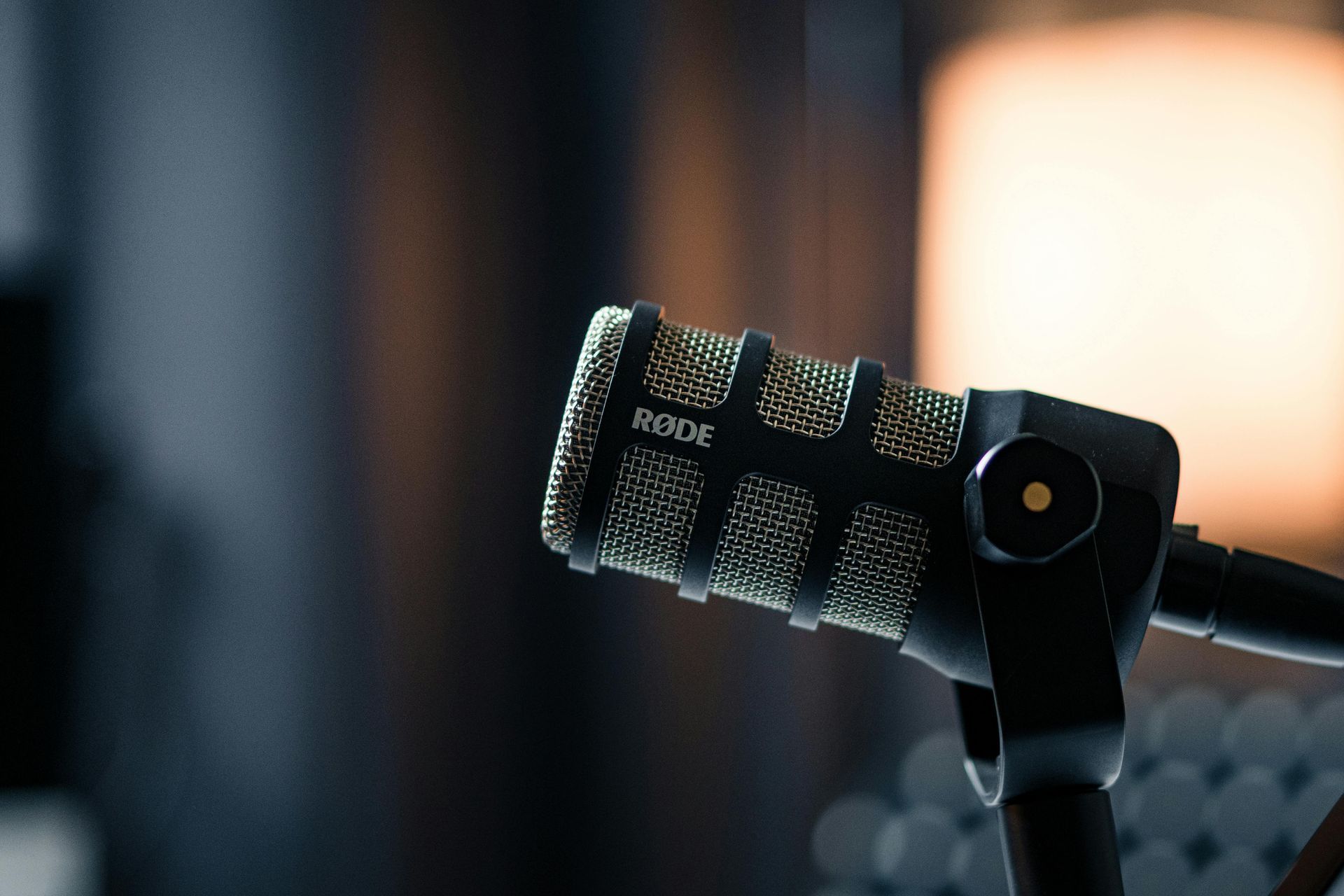 Close-up of a RODE microphone on a black stand, against a blurred studio background with soft lighting.