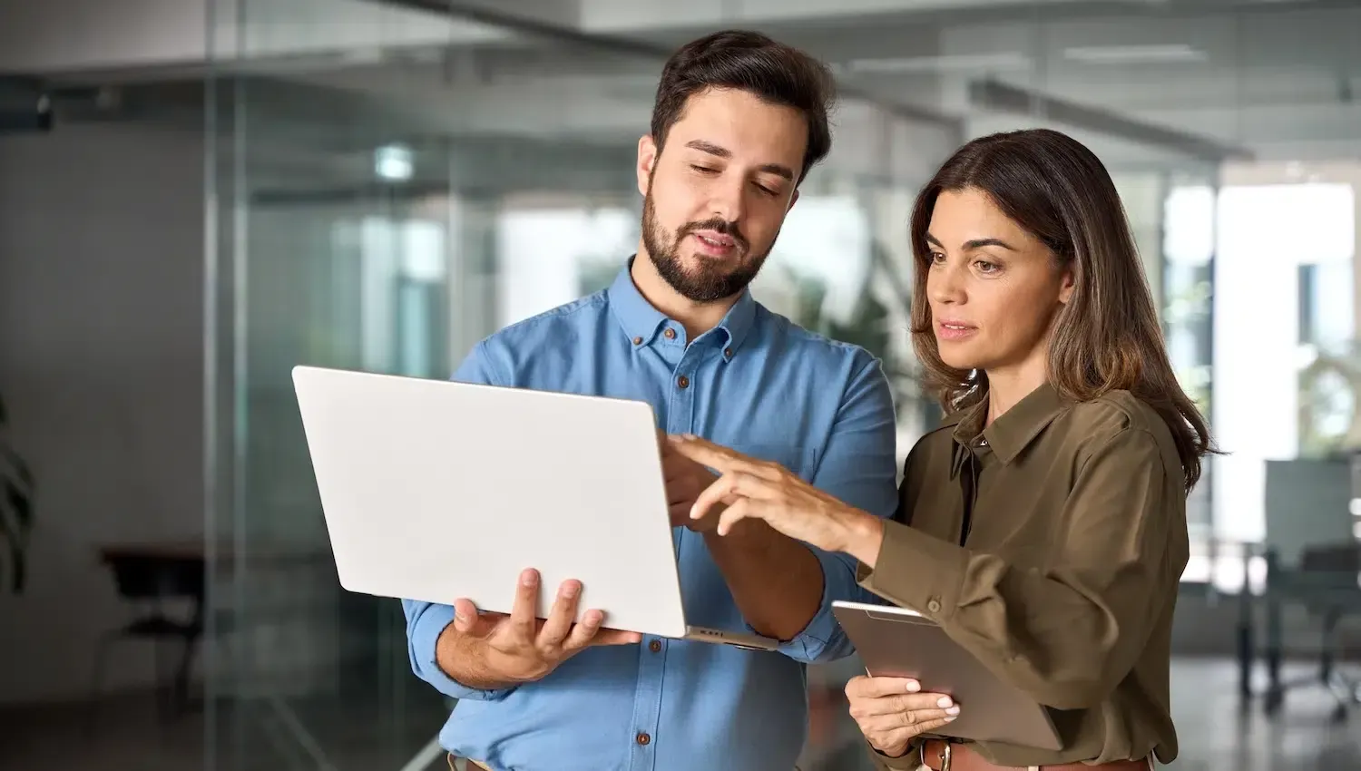 Man and woman looking at laptop screen in an office, discussing details, with a tablet.