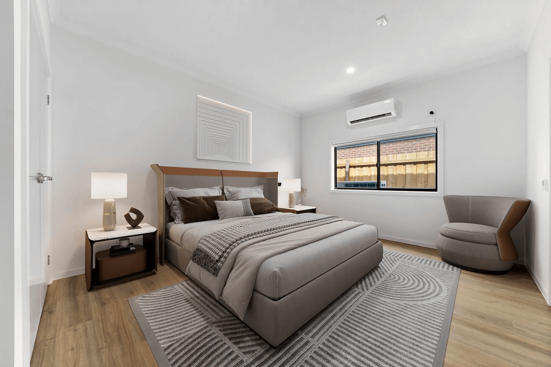 A modern bedroom at 21 Gellibrand Rd, Winter Valley, VIC 3358 features a neatly made bed with gray and brown bedding, a geometric-patterned rug, bedside table with lamp, round chair, wooden floors, and blinds letting in natural light.