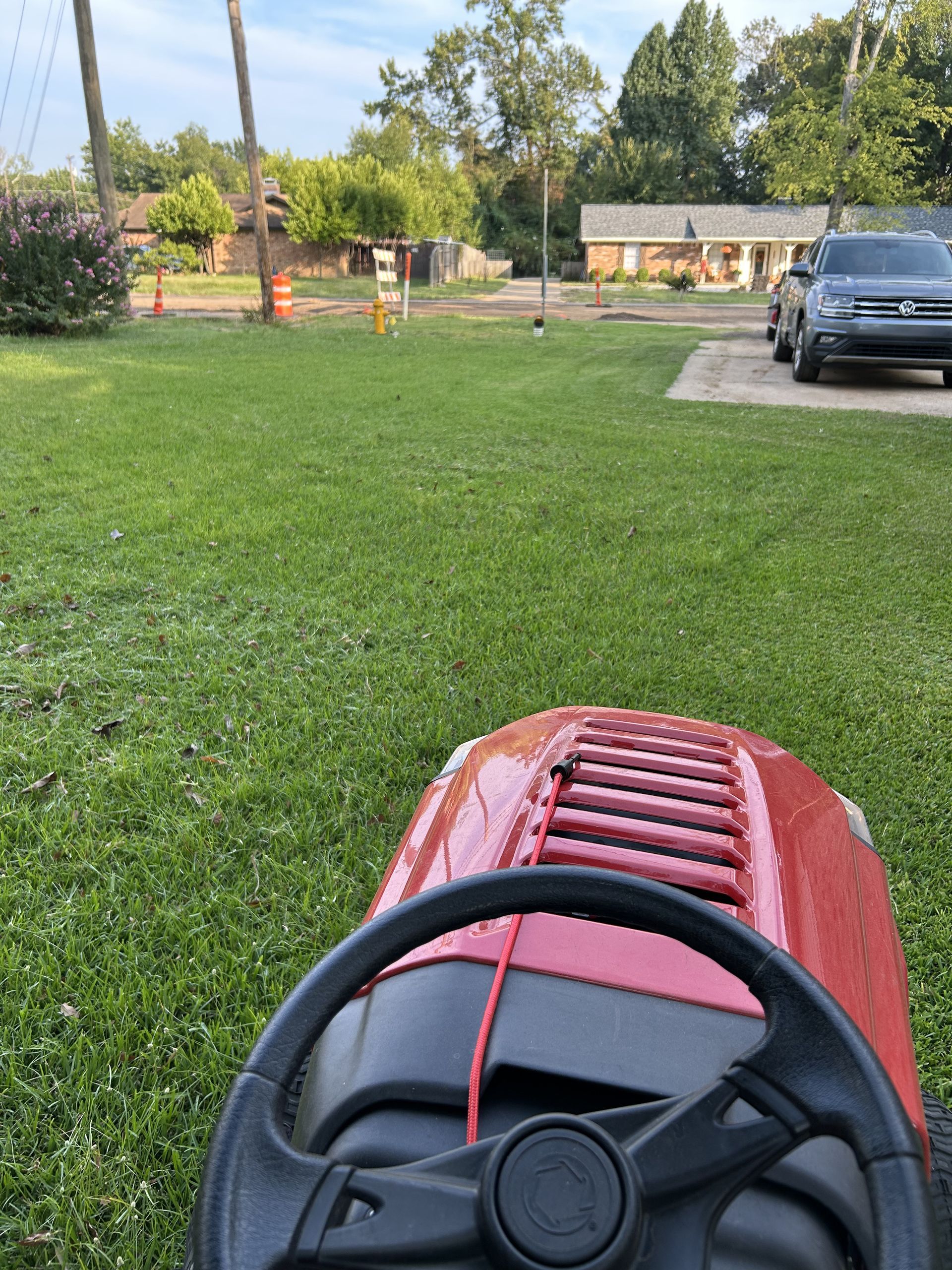 Red riding lawnmower mowing a green lawn, houses in background.