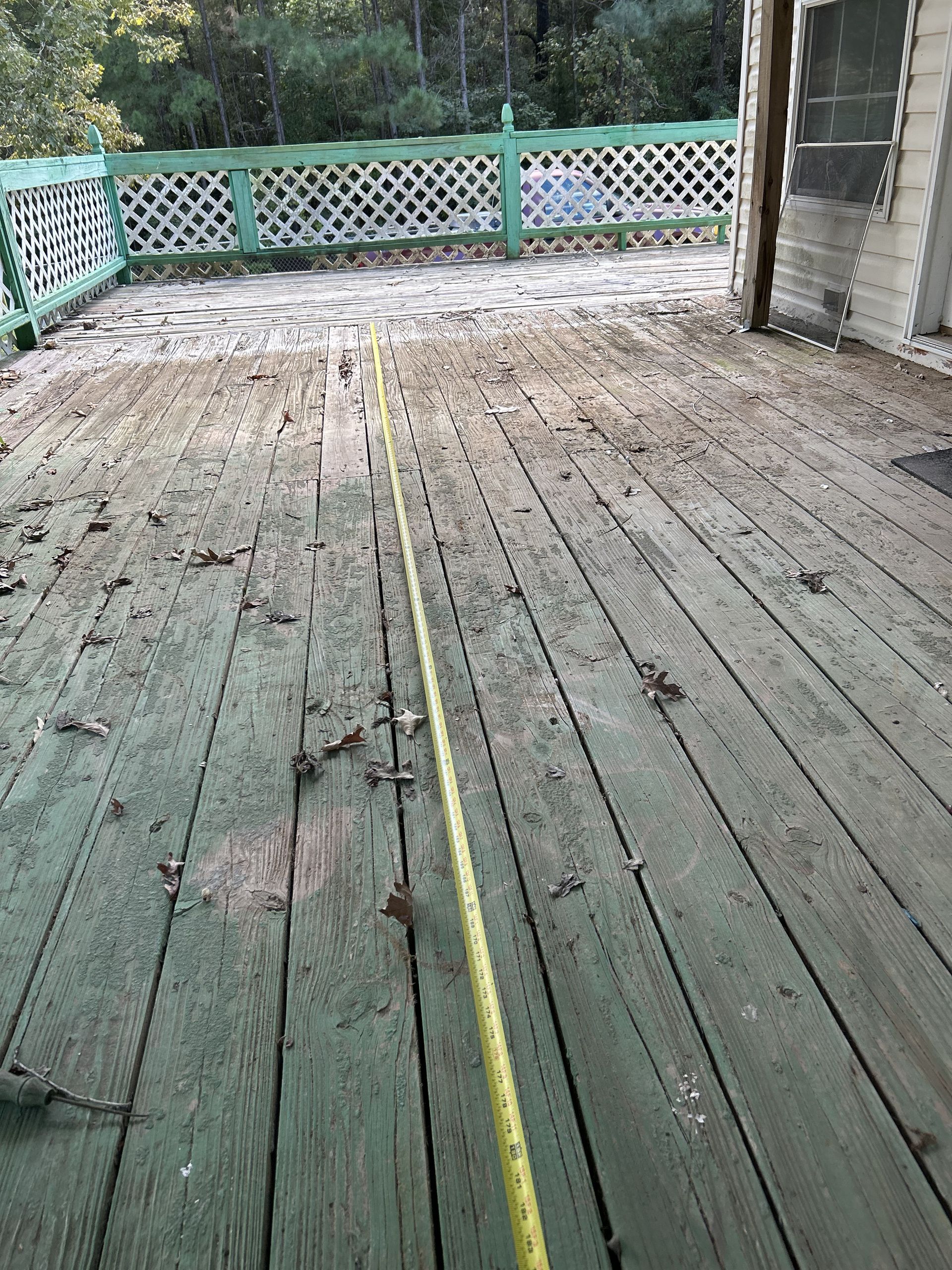 Wooden deck with green paint, debris, and a yellow measuring tape.