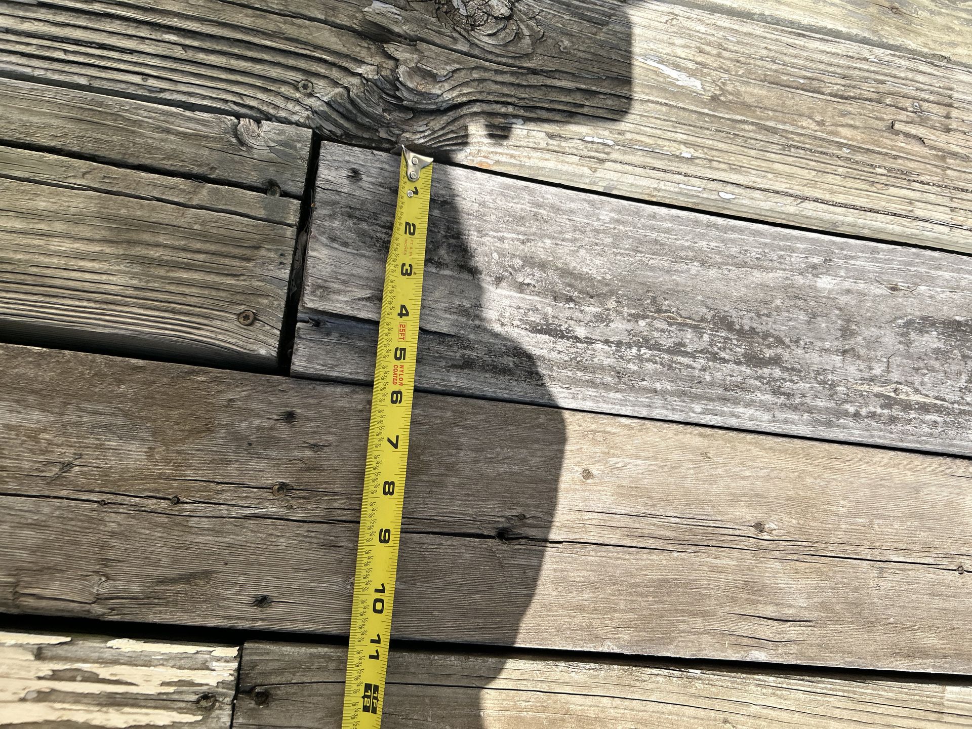 Wooden deck boards with a yellow tape measure, measuring approximately 4 inches.