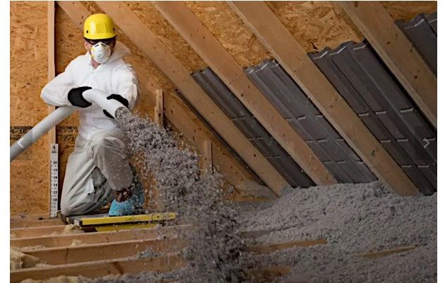 A man is blowing insulation into the attic of a house.
