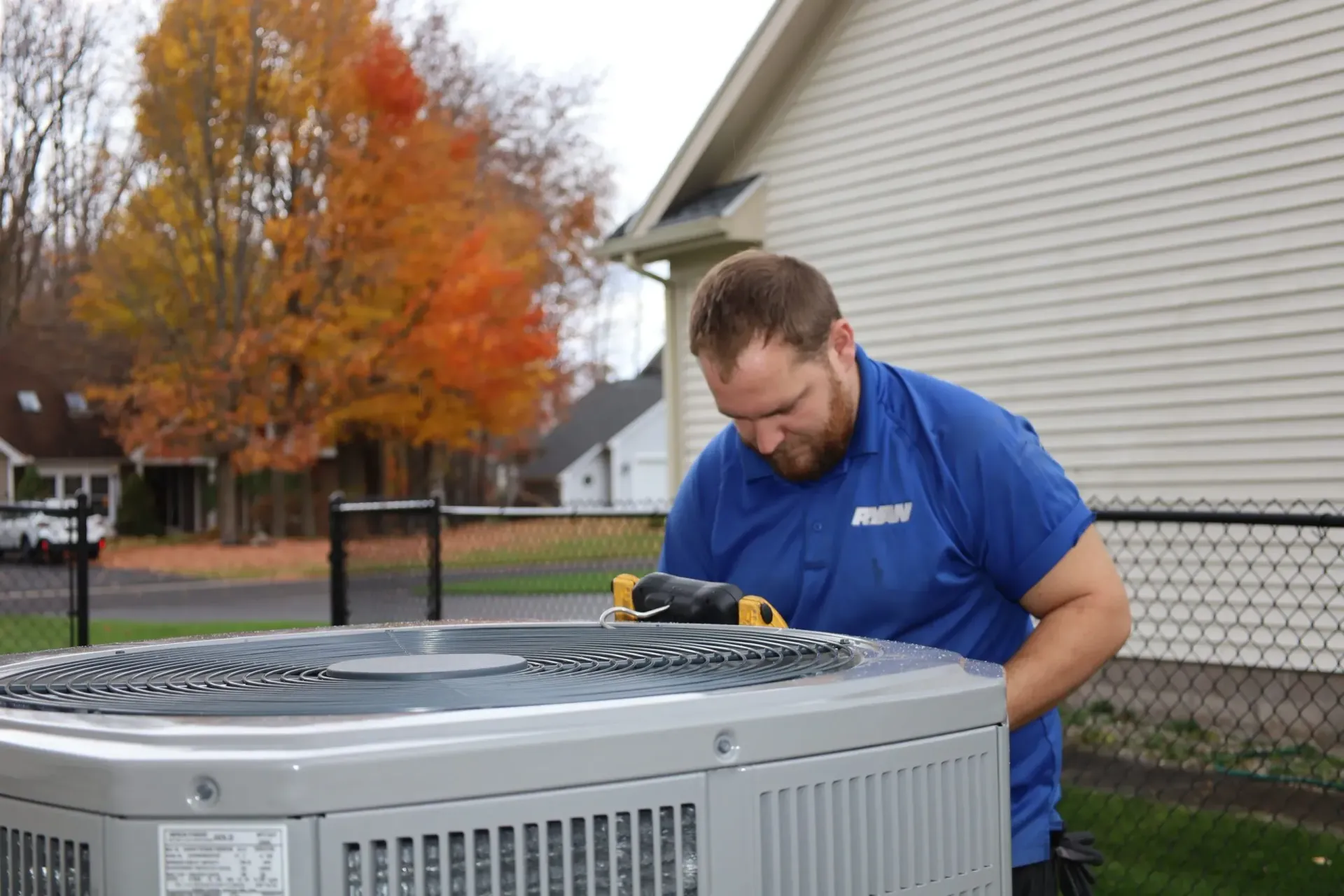A man in a blue shirt is working on an air conditioner outside of a house.