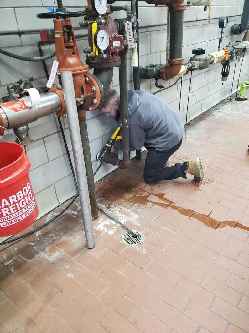 A man is kneeling down in front of pipes in a room.