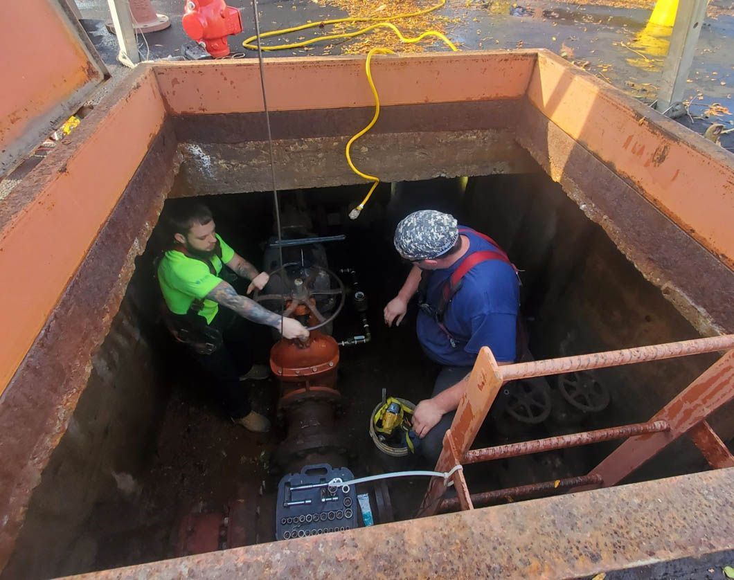Two men are working on a pipe in a hole