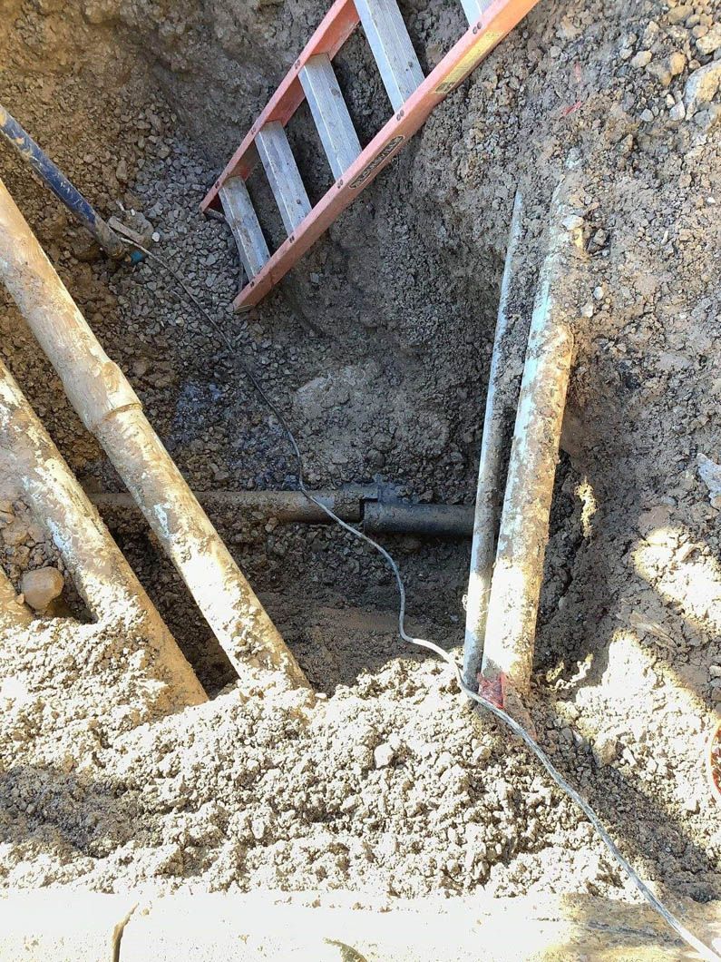 A ladder is sitting on top of a pile of dirt next to a pipe.