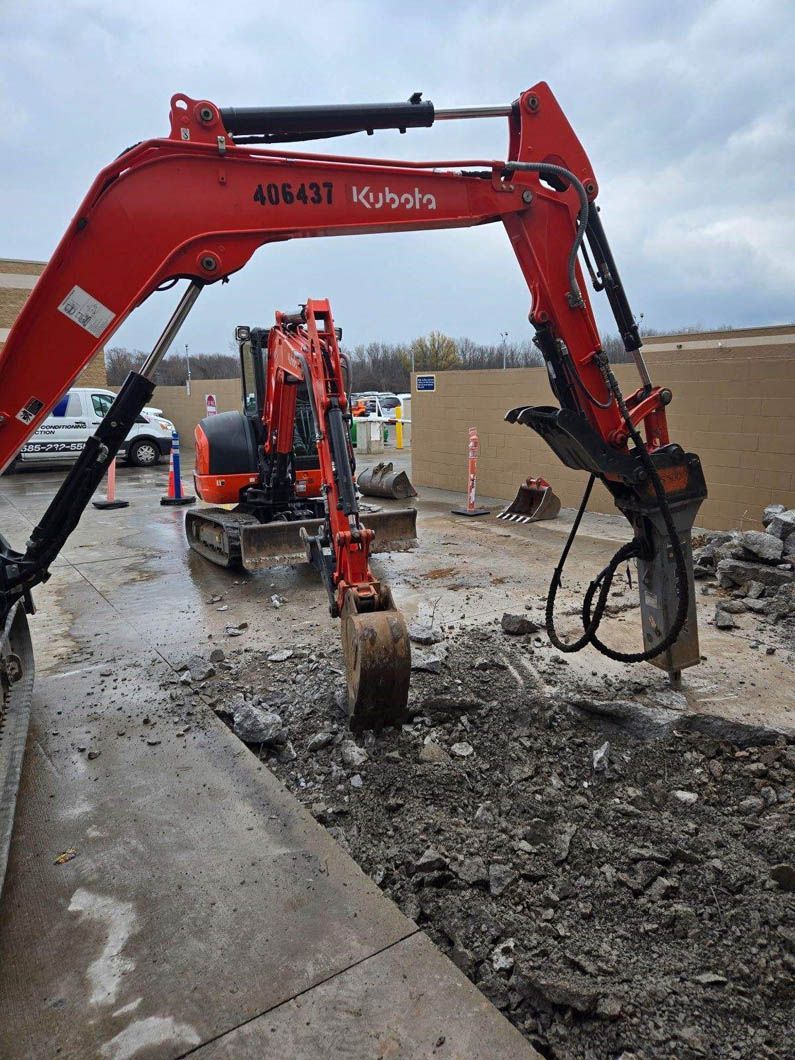 A red and black excavator is digging a hole in the ground.