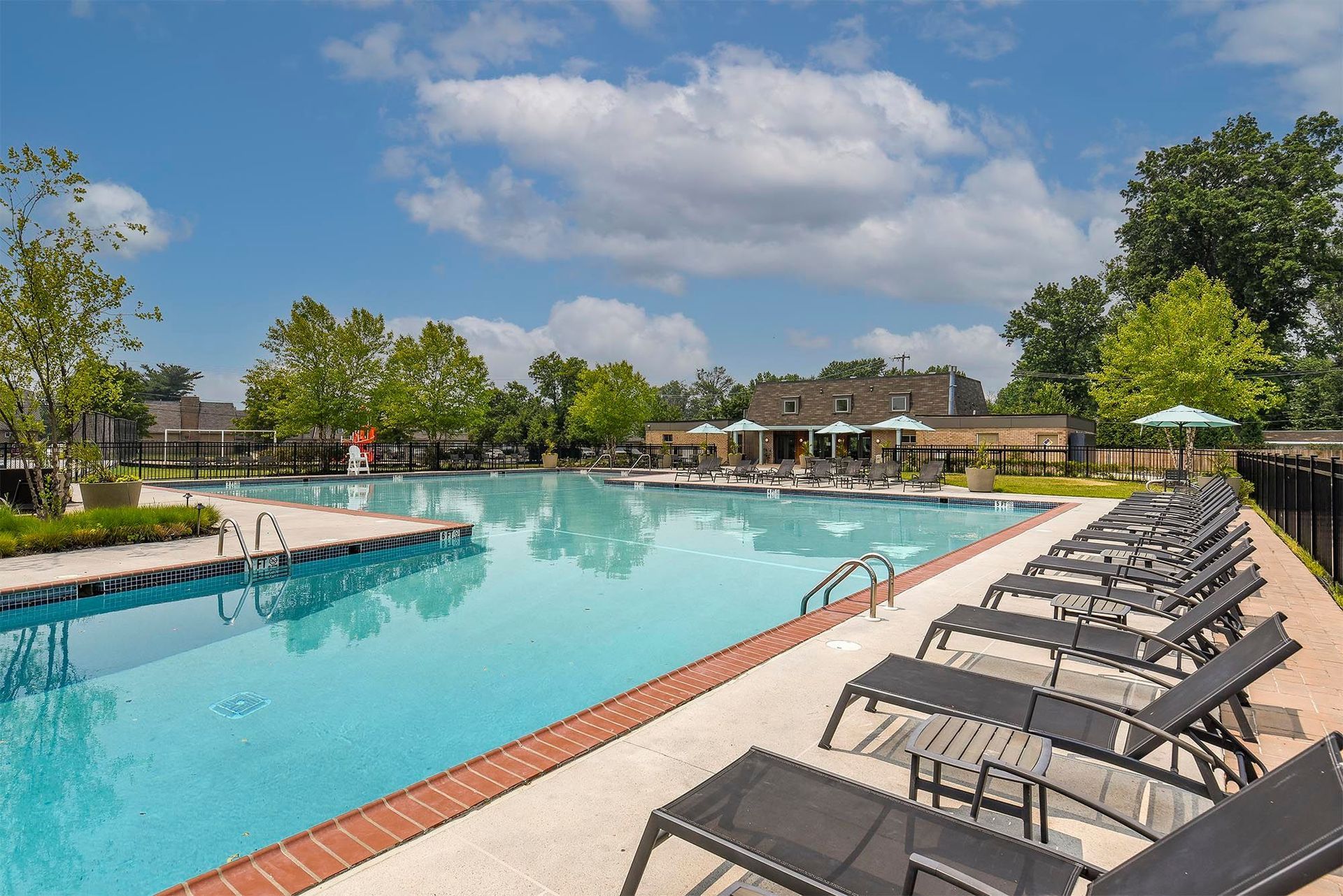 Outdoor community pool area with lounge chairs and umbrellas on a sunny day.