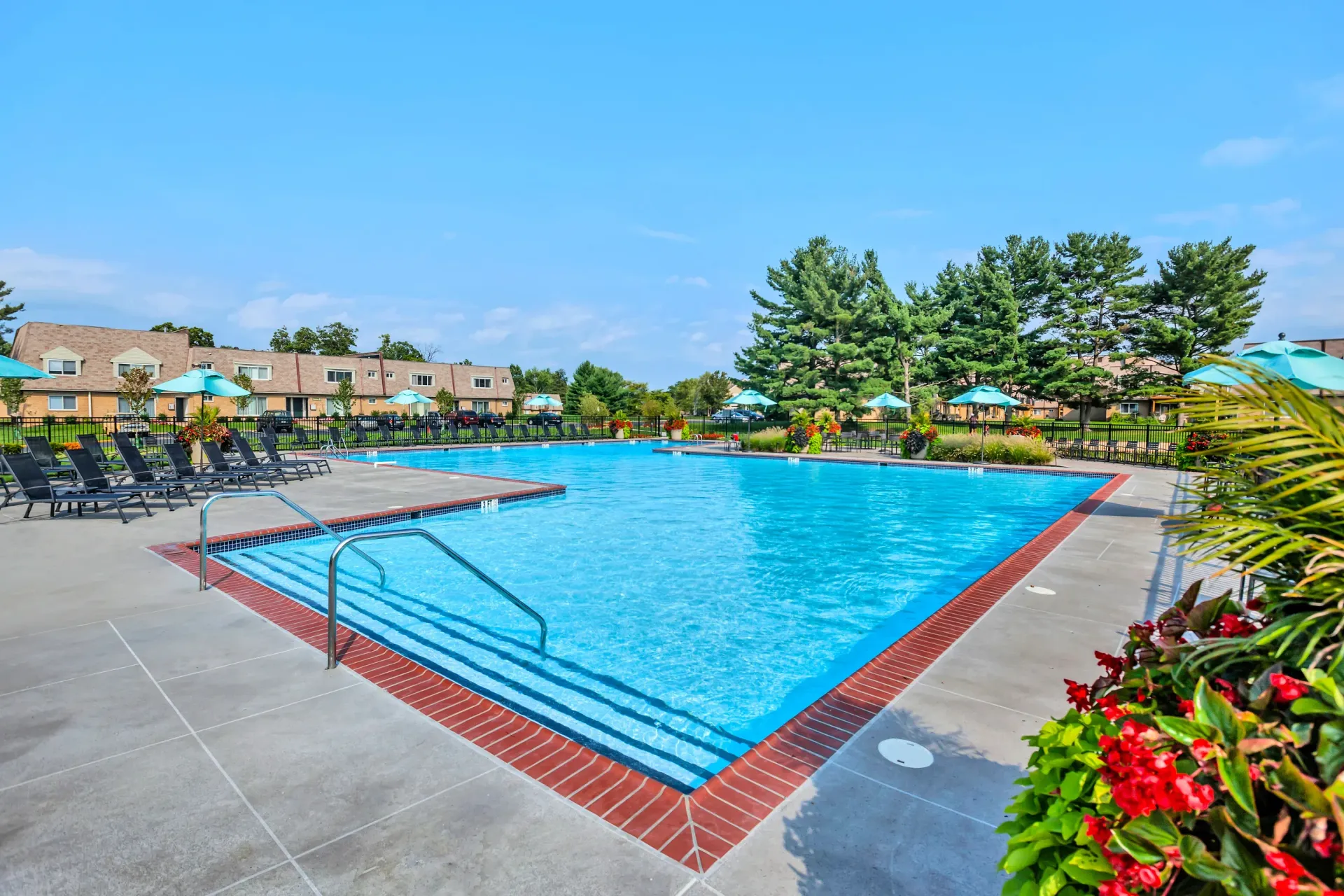 Outdoor community pool with blue water, lounge chairs, and teal umbrellas.