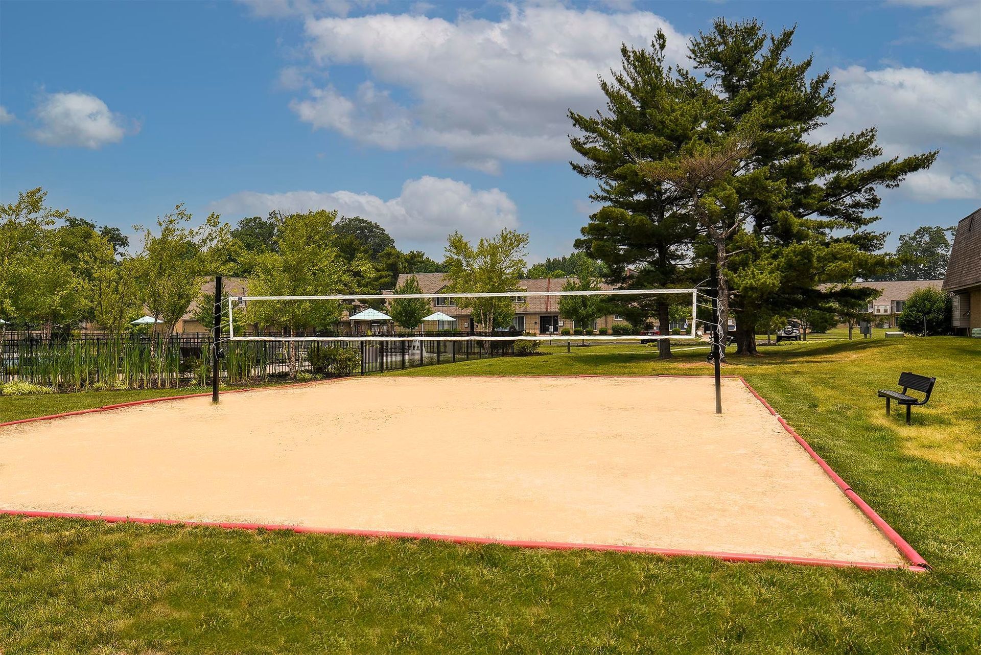 Outdoor sand volleyball court with a net, surrounded by grass and trees.