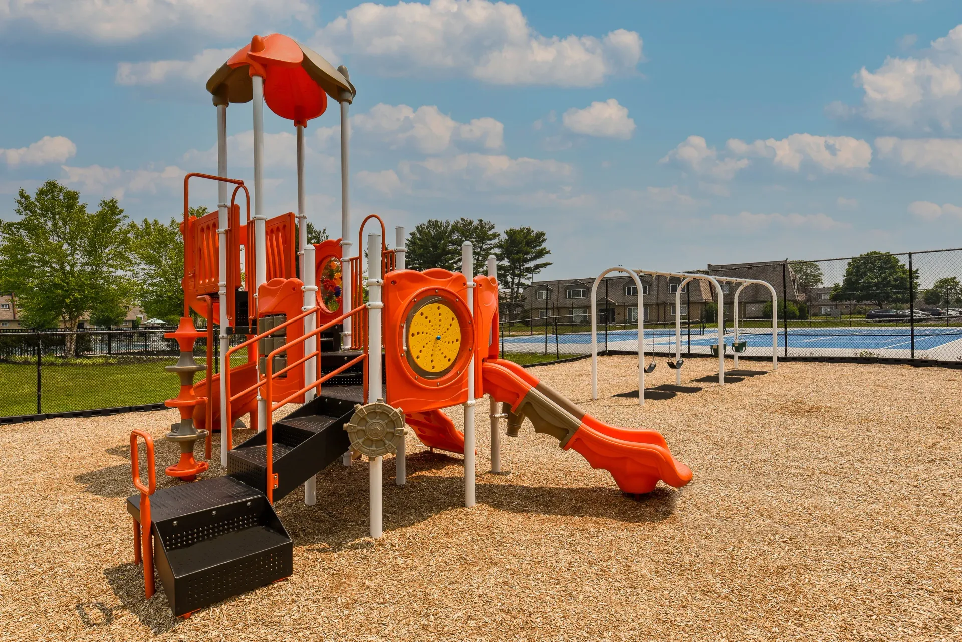 Orange playground structure with slides on gravel; fenced recreation area in the background.
