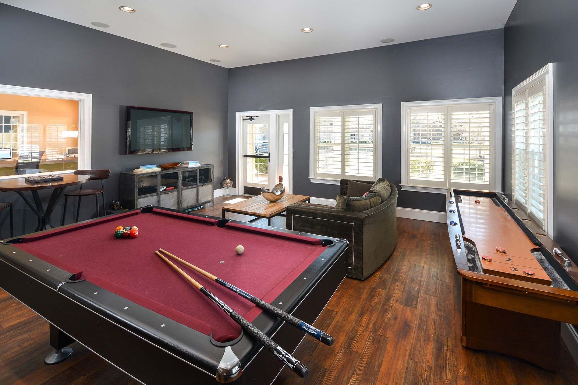 Indoor amenity room with a pool table, shuffleboard, sofa, and TV.