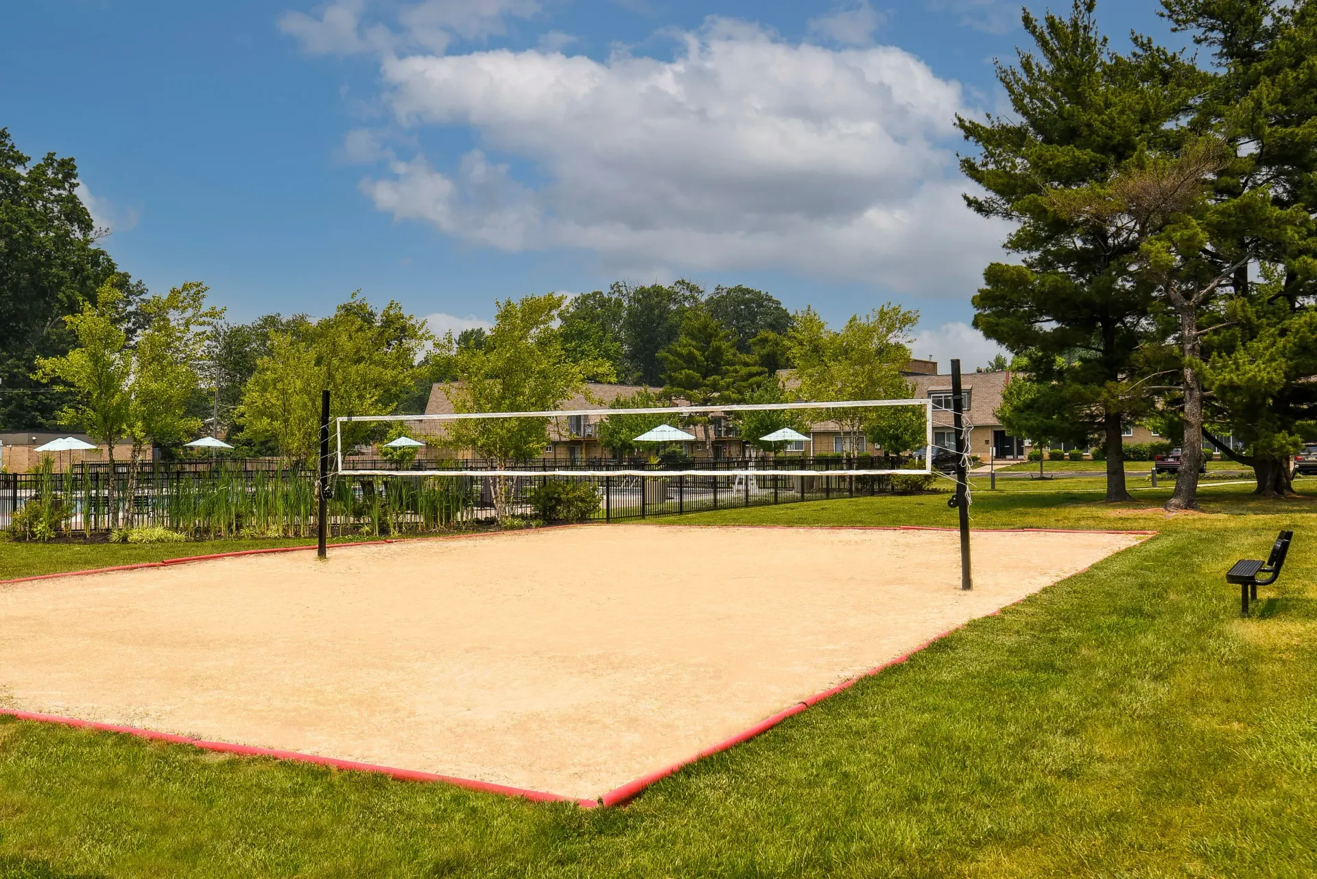 Outdoor sand volleyball court with net at apartment community, with trees and buildings in background.