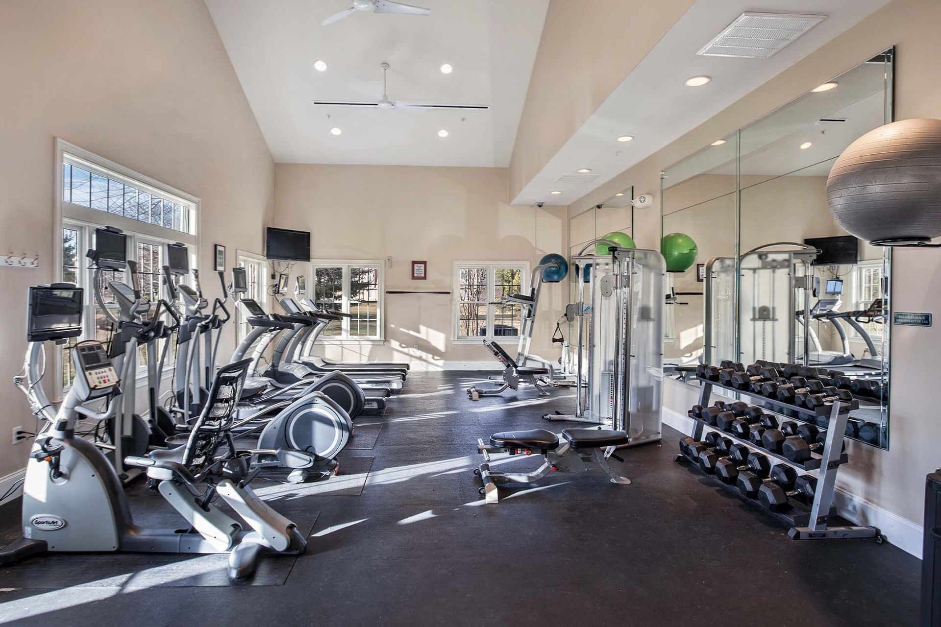 Bright community gym with cardio machines, free weights, and mirrors.